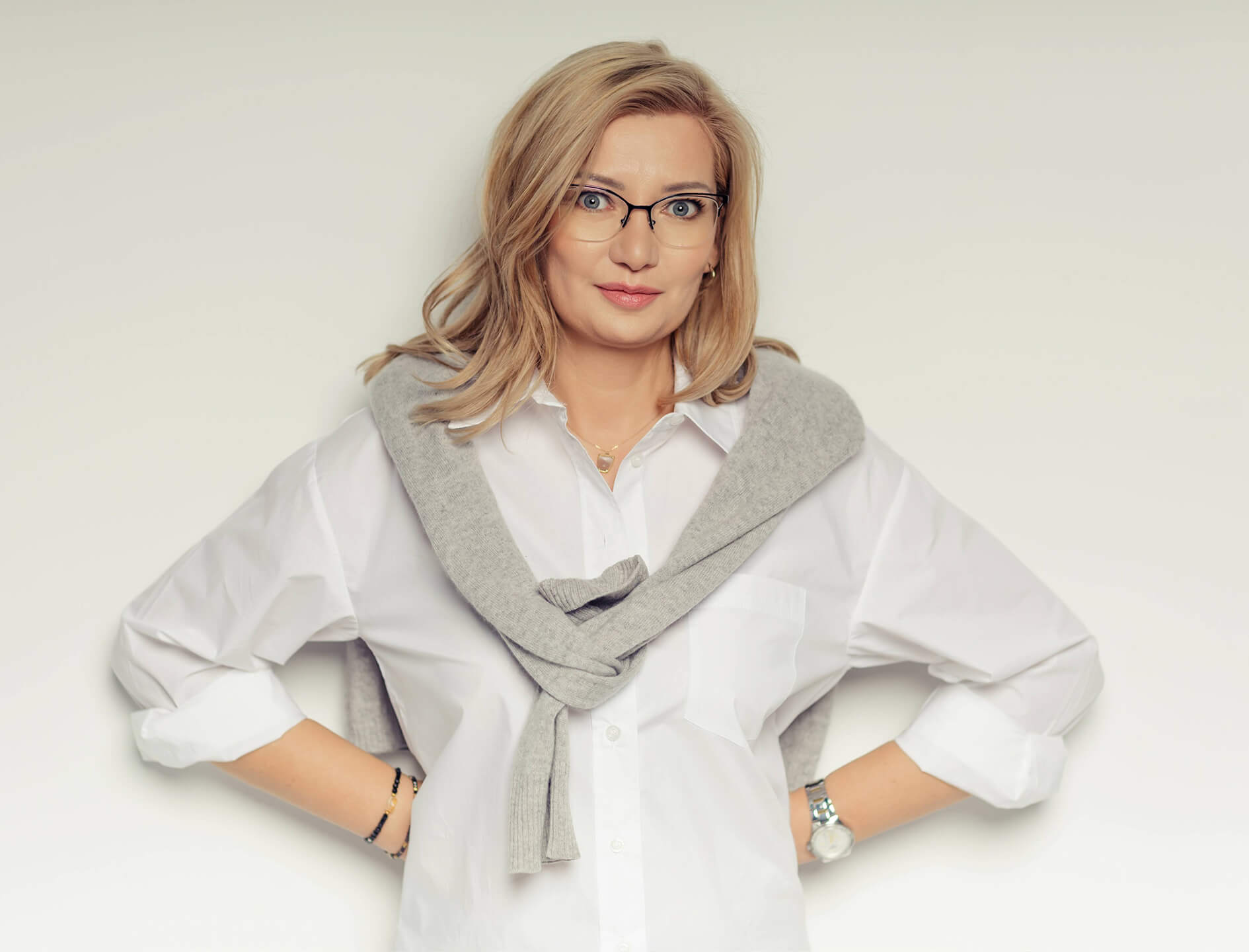 Joanna Karpeta na białym tle, z rękami założonymi na biodrach.